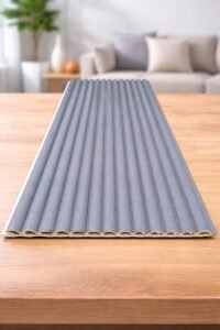 Grey fluted wall panel with vertical ribbed design displayed on a wooden table in a modern interior setting.