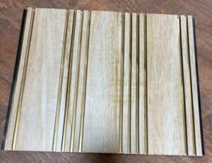 Light beige wood-textured fluted wall panel with vertical golden metallic strips for modern interior decoration.