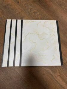 White marble finish fluted wall panel with elegant golden vein patterns and dark grey vertical grooves.